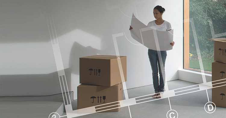 En kvinna som står upp i ett tomt rum med några kartonger och tittar på en ritning