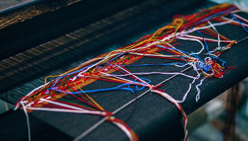 Närbild på trådar i vävstols som systematiskt och strukturerat väv still tyg